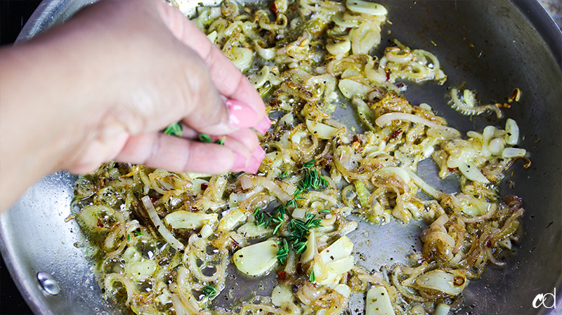 adding fresh thyme to shallots and garlic